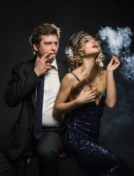 A couple of smoker glamour gangsters, a man and woman with cigarettes on black background with smoke
