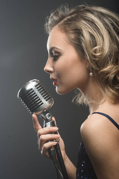 Portreit of sexy young girl singer singing with silver retro microphone on black background