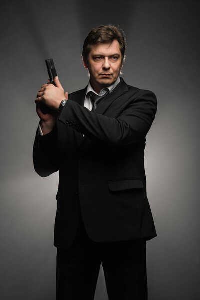 Handsome middle aged detective man with gun on dark background with stage smoke