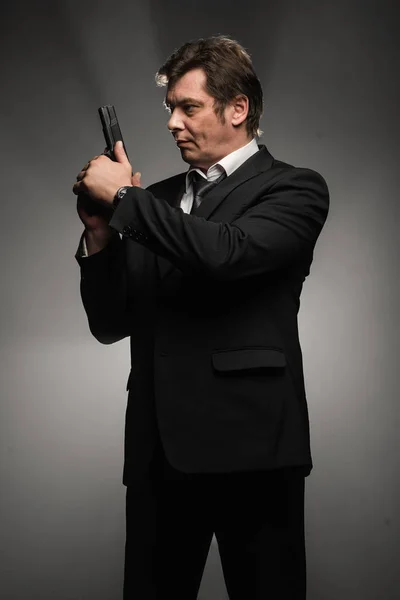 Handsome middle aged detective man with gun on dark background with stage smoke