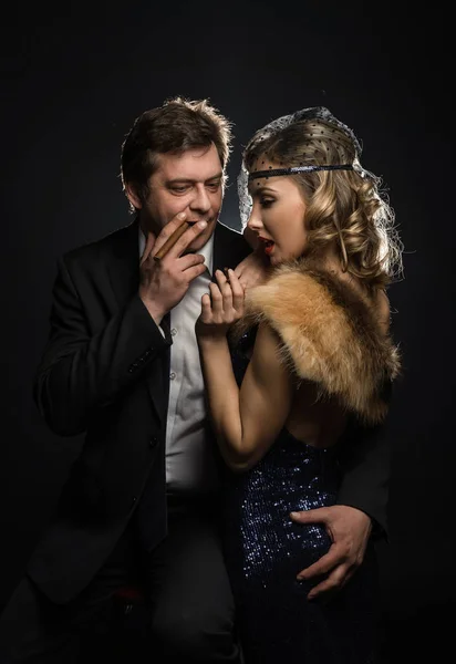 A couple of smoker glamour gangsters, a man and woman with cigarettes on black background with smoke