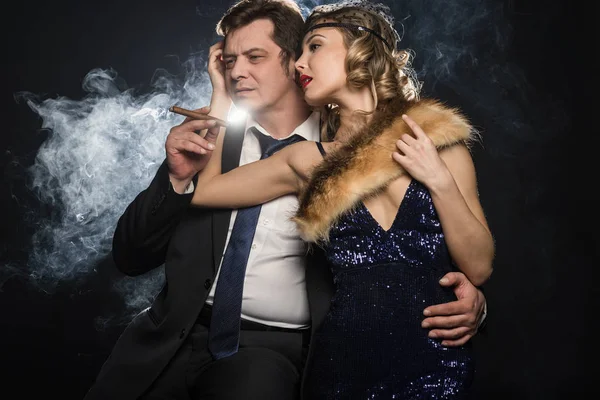 A couple of smoker glamour gangsters, a man and woman with cigarettes on black background with smoke