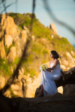 Düğün elbise gelin Asya dağlara karşı günbatımında oturur.