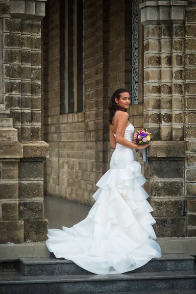 the bride standing against the wall with a wedding bouquet of flowers