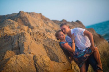Okyanusa karşı gün batımında güzel birkadın kayalarda kucaklayan bir adam