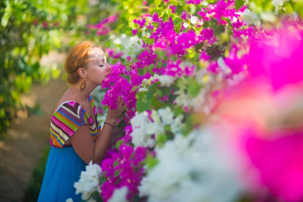 Genç güzel kadın güzel çiçek kokusu nefes alır. Kız mavi bir elbise giymiş, mor ve beyaz çiçekler tarafından çevrilidir.