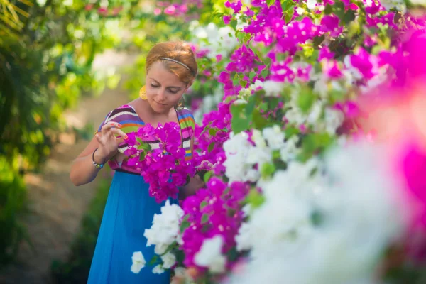 Güzel bir kadın güzel çiçek kokusu nefes alır. Kız mavi bir elbise giymiş, mor ve beyaz çiçekler tarafından çevrilidir.