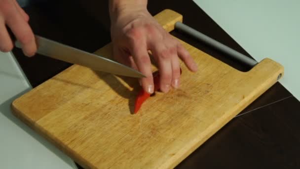 Skivning röd chili peppar. En man skär paprika på en träskiva — Stockvideo