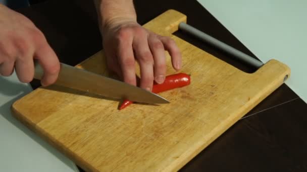 Нарізати перець червоного чилі. Чоловік розрізає перець на дерев'яній дошці — стокове відео