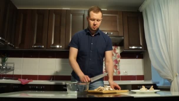 Мужчина-повар наливает нарезанные грибы в миску — стоковое видео