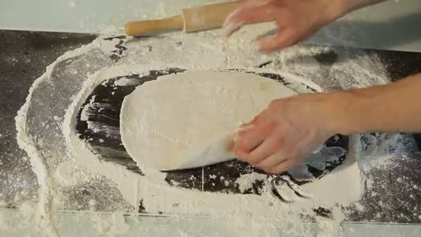 Мужчина катит тесто на кухонный стол скалкой. . — стоковое видео