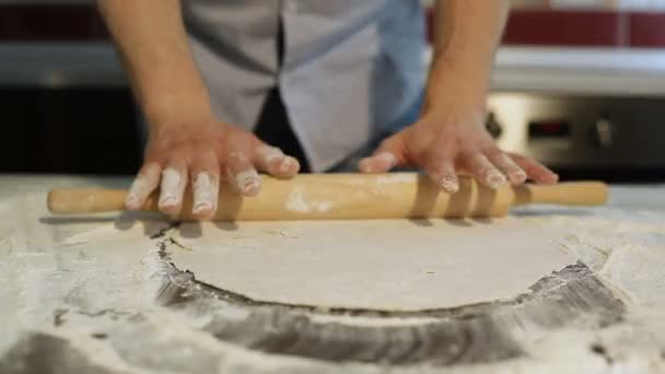 L'homme roule la pâte sur la table de cuisine avec un rouleau à pâtisserie . — Video