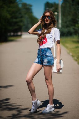 Güzel genç hippi kız Park poz güneş gözlüğü. Kız birilerini bekliyor.