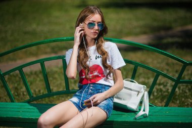 Genç güzel kız parkta bir bankta oturan kulaklıklar müzik dinlemek.