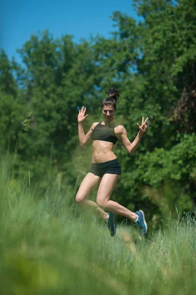 Genç kadın ağaçlar arka plan üzerinde atlama. Kızı sporda devreye girer.