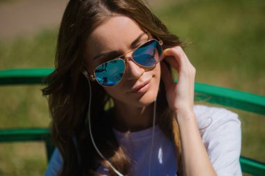 Genç güzel kız parkta bir bankta oturan kulaklıklar müzik dinlemek.