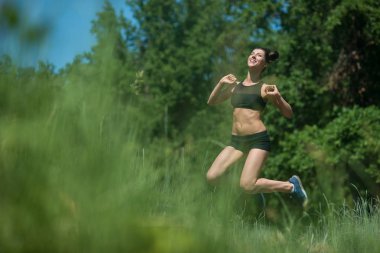 Genç kadın ağaçlar arka plan üzerinde atlama. Kızı sporda devreye girer.