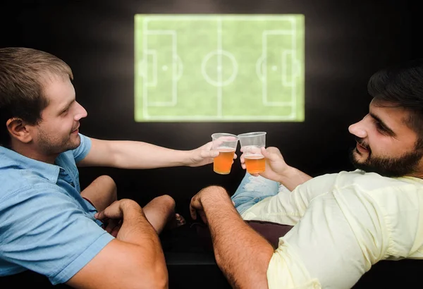 Los aficionados masculinos ven fútbol en la televisión y beben cerveza. Amigos tienen un gran tiempo bebiendo cerveza . — Foto de Stock