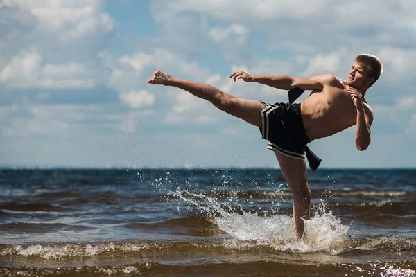 Arka plan suda ayakta denizin üzerinde tekme genç bir asker. Açık havada egzersiz
