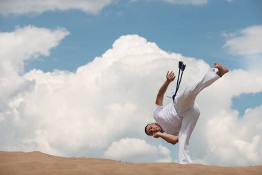 Trenler capoeira gökyüzü artalanları üzerinde genç adam. Kavramı kişi, yaşam tarzı ve spor hakkında. Bir erkek dövüş gerçekleştirir tekme