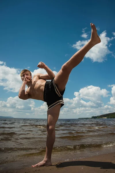 Kickboxer kicks in the open air in summer against the sea. Combat sport