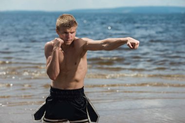 Kaslı erkek savaşçı deniz artalanları üzerinde eğitim. Açık havada boksör trenler