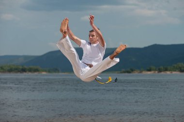 Trenler capoeira gökyüzü artalanları üzerinde genç adam. Kavramı kişi, yaşam tarzı ve spor hakkında. Bir erkek gerçekleştirir dövüş olarak atlama tekme