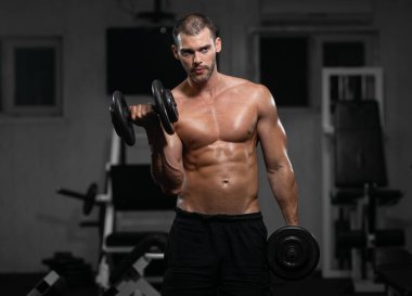 Bir adam spor salonunda eğitiyor. Onun pazı pompa dambıl, trenlerle atletik erkek