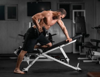 Bir adam spor salonunda eğitiyor. Onun pazı pompa dambıl, trenlerle atletik erkek