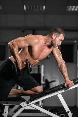 Bir adam spor salonunda eğitiyor. Onun pazı pompa dambıl, trenlerle atletik erkek
