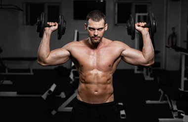 Spor eğitim dumbbells ile güzel kaslı adam, adam onun deltoid kas pompalar.