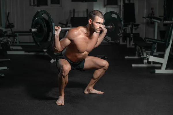 Handsome weightlifter lifting barbells with Squats. Male training with barbell, pumping legs