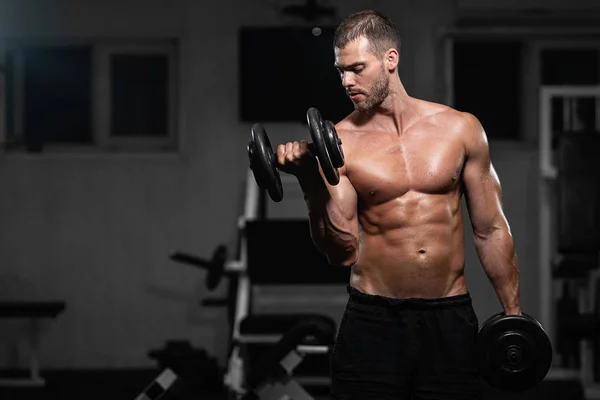 Bir adam spor salonunda eğitiyor. Onun pazı pompa dambıl, trenlerle atletik erkek