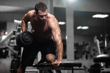 Bir adam spor salonunda eğitiyor. Onun pazı pompa dambıl, trenlerle atletik erkek