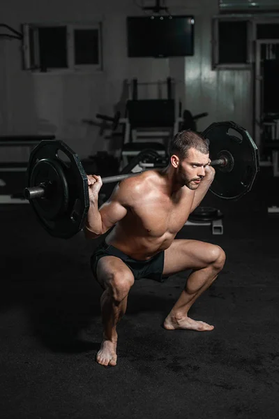 Handsome weightlifter lifting barbells with Squats. Male training with barbell, pumping legs