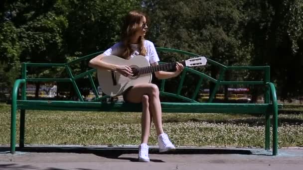 Bella ragazza hipster che suona la chitarra all'aperto nel parco — Video Stock