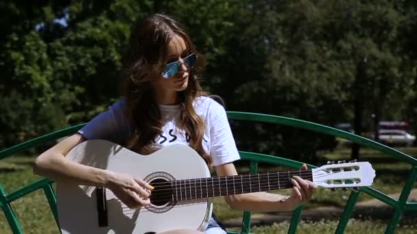 Όμορφη νεαρή hipster κορίτσι παίζει κιθάρα σε εξωτερικούς χώρους στο πάρκο — Αρχείο Βίντεο