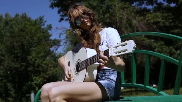 Красивая молодая хипстерша играет на гитаре в парке — стоковое видео