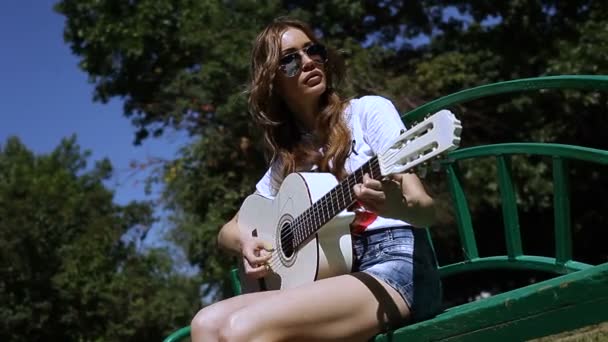 Mooie jonge hipster meisje gitaarspelen buiten in het Park — Stockvideo