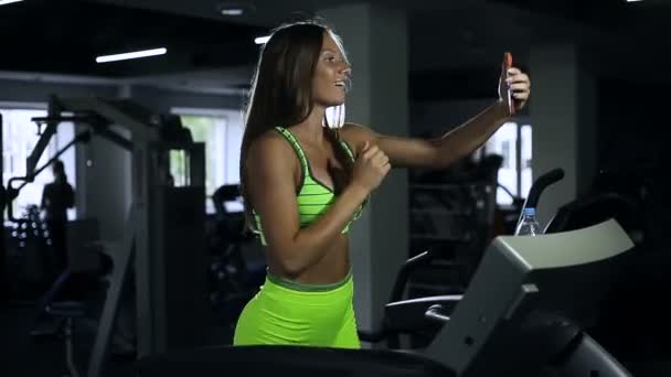 Ragazza prende un selfie in palestra, la donna viene fotografata sul tapis roulant — Video Stock