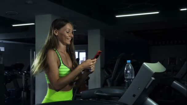 Mädchen macht Selfie im Fitnessstudio, Frau wird auf dem Laufband fotografiert — Stockvideo