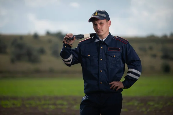 Поліцейський у формі зі стрижнем у руці на фоні сільського пейзажу — стокове фото