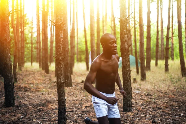 Um afro-americano a correr na floresta ao pôr-do-sol. Jogadas de atleta — Fotografia de Stock