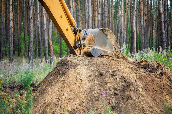 Экскаватор проводит земляные работы, копая землю ведром.
