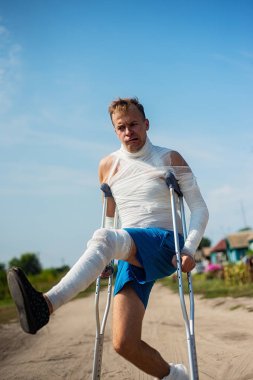 Bandaj kırsal kesimde yolda yürürken, eğleniyor ve palyaçoluk yapım koltuk değneği genç bir adam