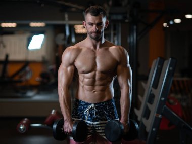 Güzel genç kaslı adam dumbbells ile el spor salonunda poz