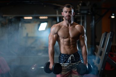 Güzel genç kaslı adam dumbbells ile el spor salonunda poz