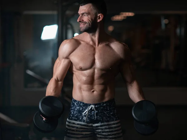 Handsome young muscular man exercising with dumbbells. Guy trains his bicep