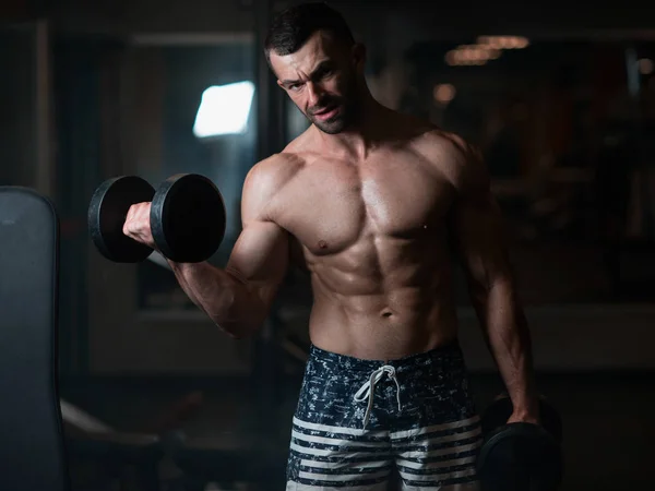Handsome young muscular man exercising with dumbbells. Guy trains his bicep