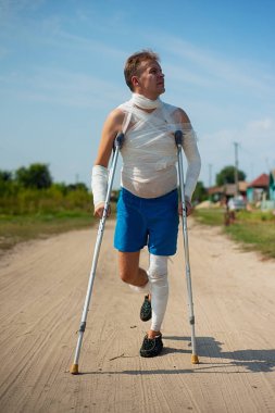 Bandaj kırsal kesimde yolda yürürken, eğleniyor ve palyaçoluk yapım koltuk değneği genç bir adam
